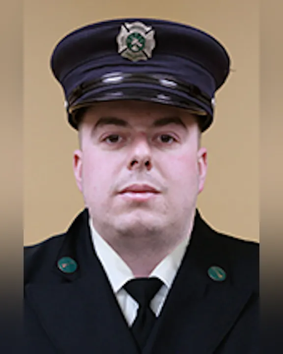 Kyle Stanley portrait. He is wearing a dark uniform and hat with a fire department insignia.