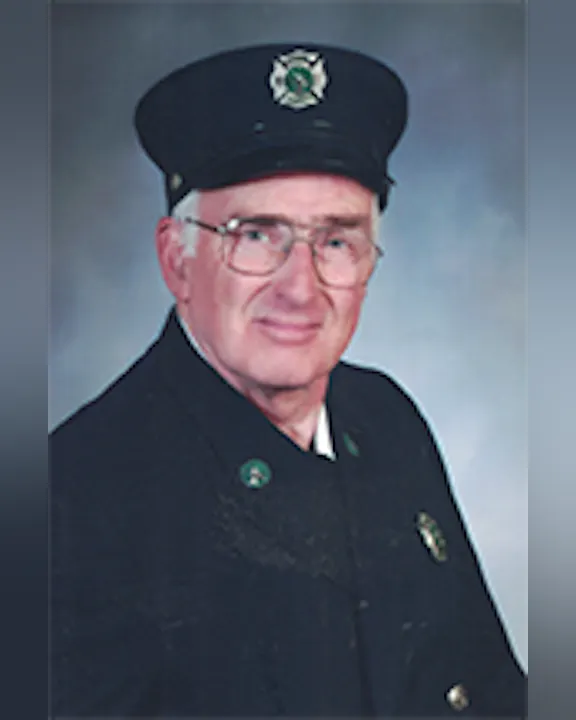 Alan Archer in a uniform with a cap, wearing glasses, posing for a portrait.