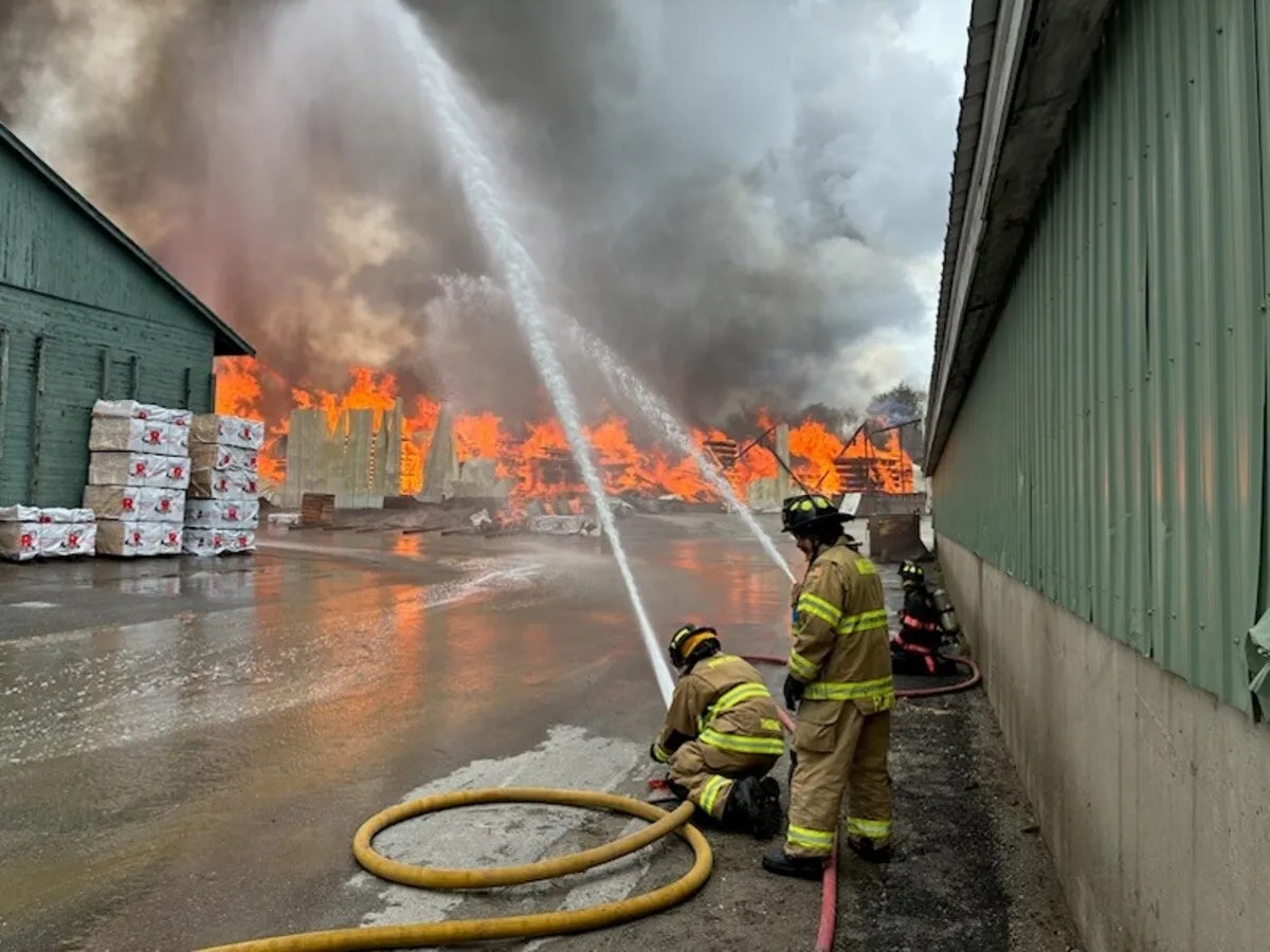 Firefighters are battling a large blaze at a structure, using hoses to control the flames and protect nearby areas.