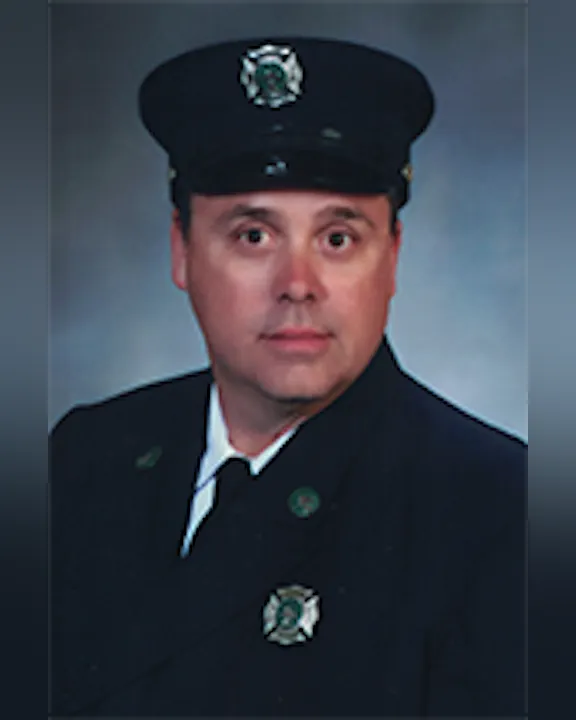 Peter Ferstler in a dark uniform and hat, likely a firefighter, poses for a formal portrait.