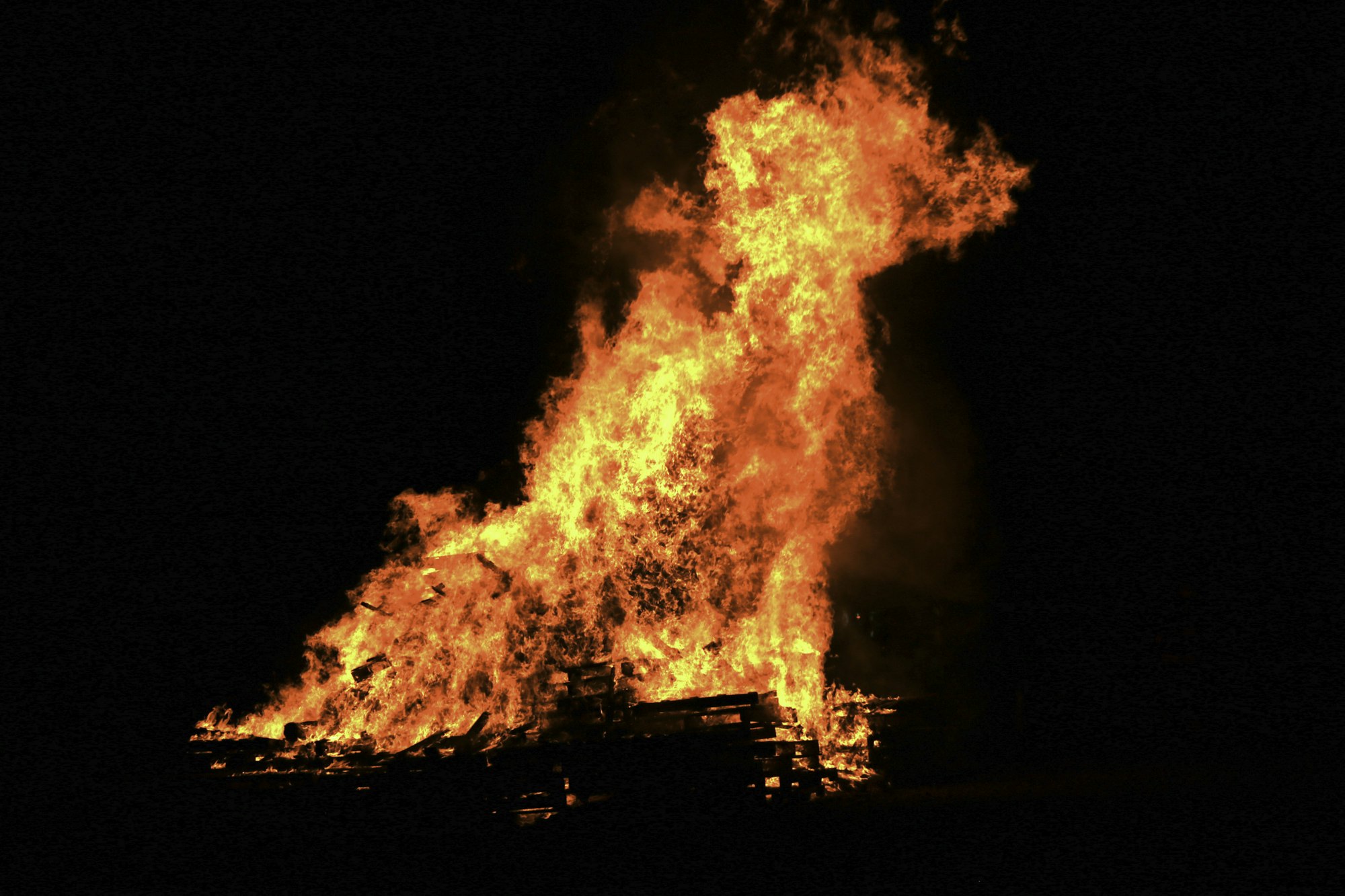 A large fire at night, with flames consuming what appears to be a pile of debris or wood.