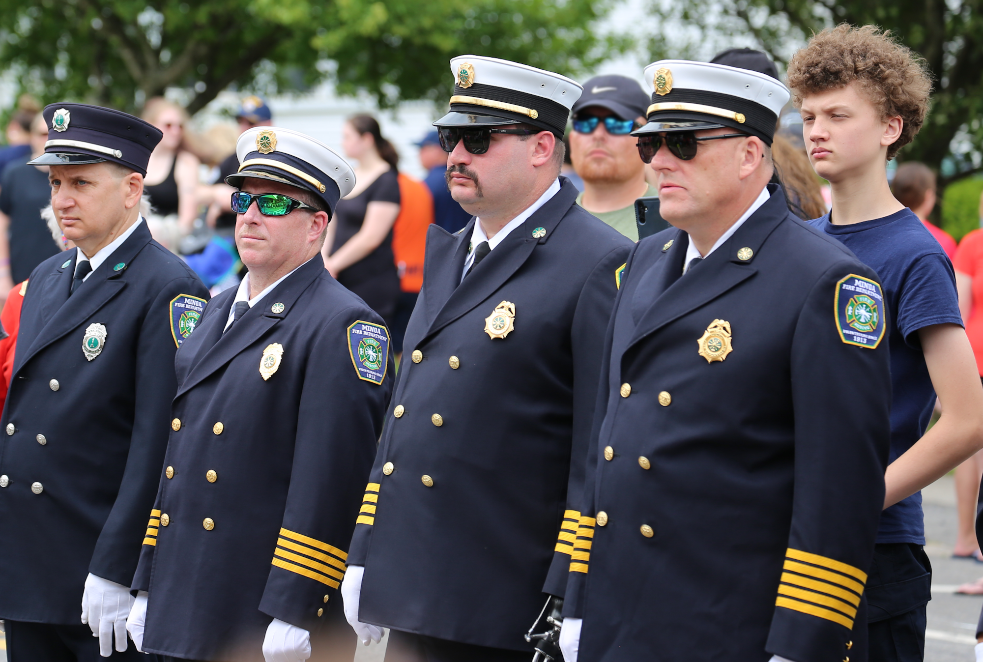 A group of uniformed officers stand in neat rows during a ceremony, with some onlookers in the background.