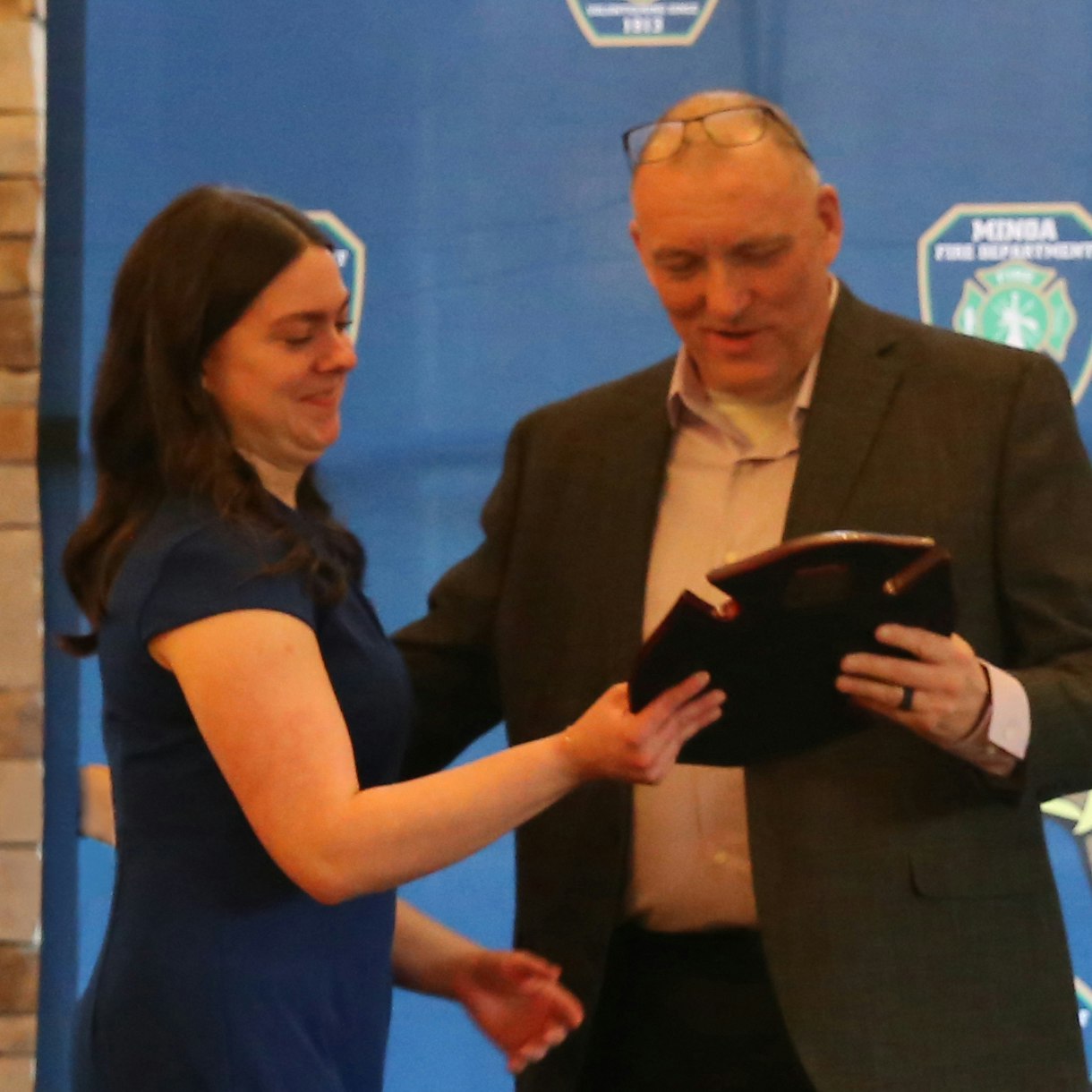 A woman and a man are engaged in a presentation, likely receiving or handing over an award or recognition at an event.