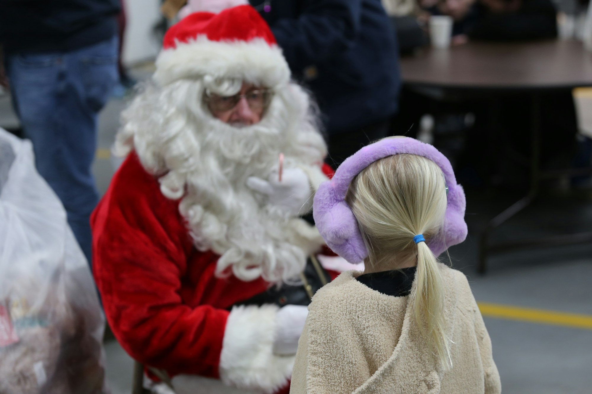 Santa Claus talking to a child wearing earmuffs indoors.