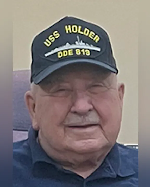Wayne Konseck wearing a cap with "USS HOLDER DDE 819" and a ship silhouette printed on it.