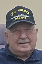 Wayne Konseck wearing a cap with "USS HOLDER DDE 819" and a ship silhouette printed on it.