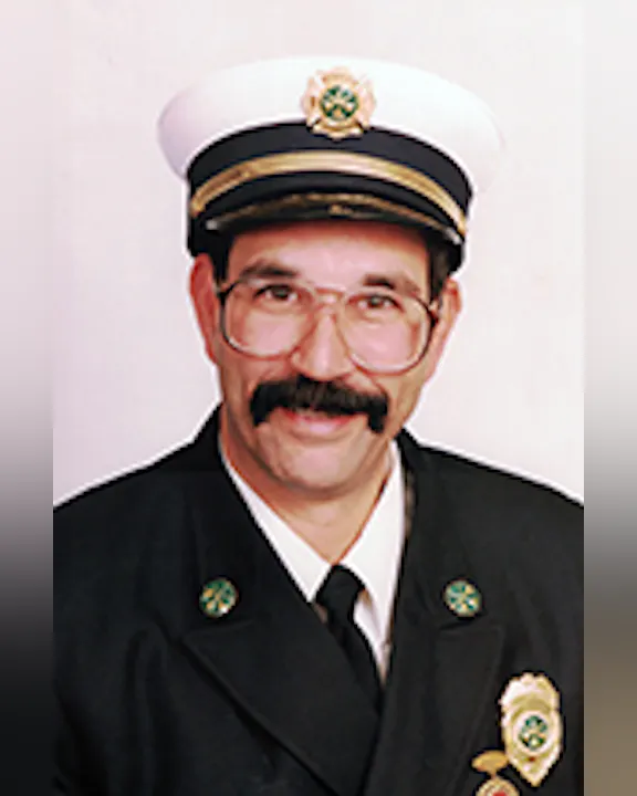 Steven Giarusso in a formal uniform with a white hat and glasses, featuring badges on the jacket.