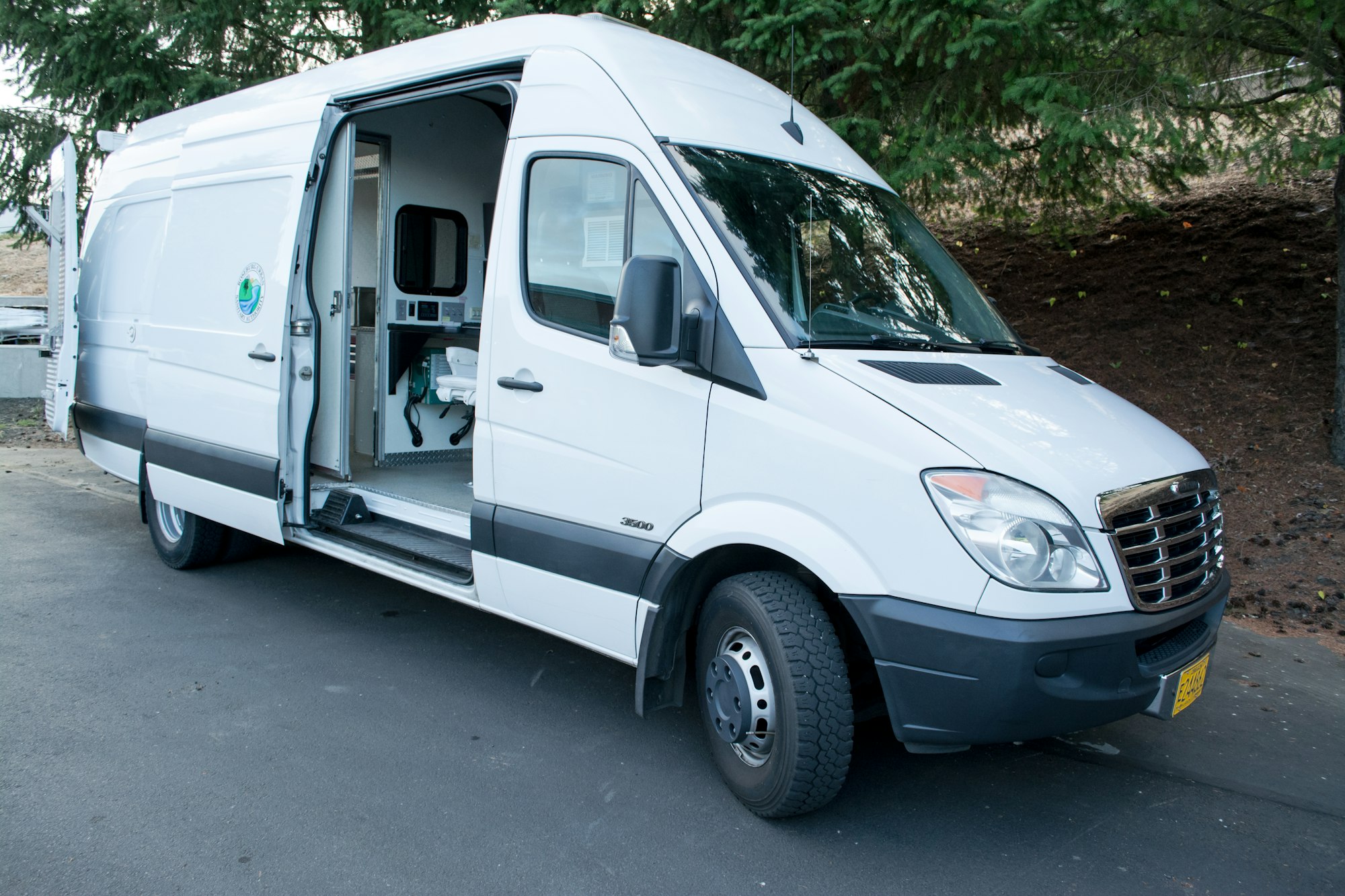 A white cargo van with an open side door, revealing a shelved interior with equipment.