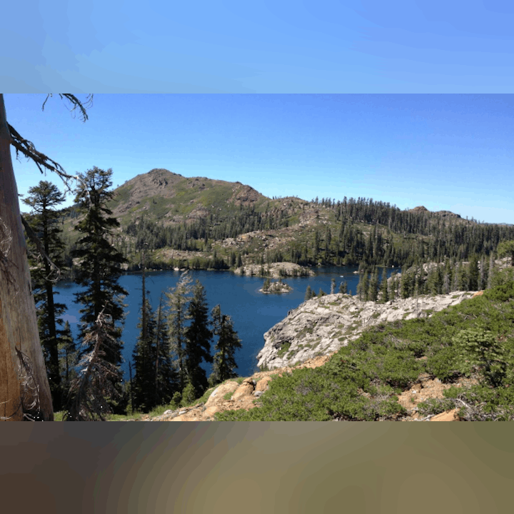 A serene mountain landscape with a lake, surrounded by lush greenery and rocky terrain under a clear blue sky.
