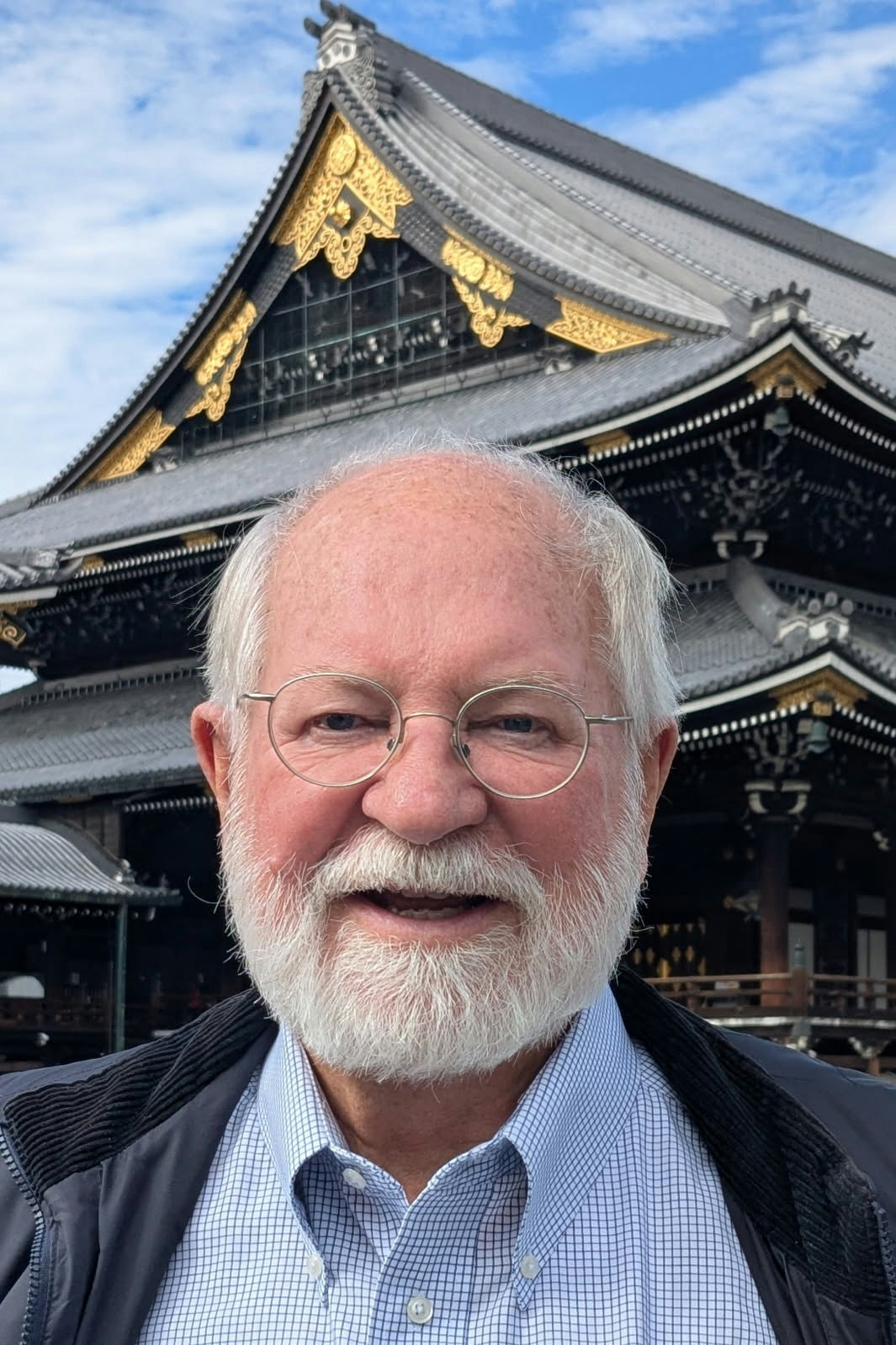 A person with glasses and a beard stands in front of a traditional Japanese temple with ornate gold detailing.