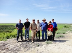 A group of seven people standing outdoors on a clear day with greenery in the background.