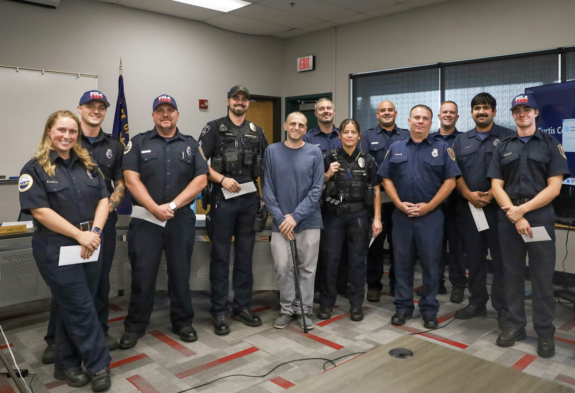 A group of firefighters and police officers posing together indoors, one person holds a walking cane.