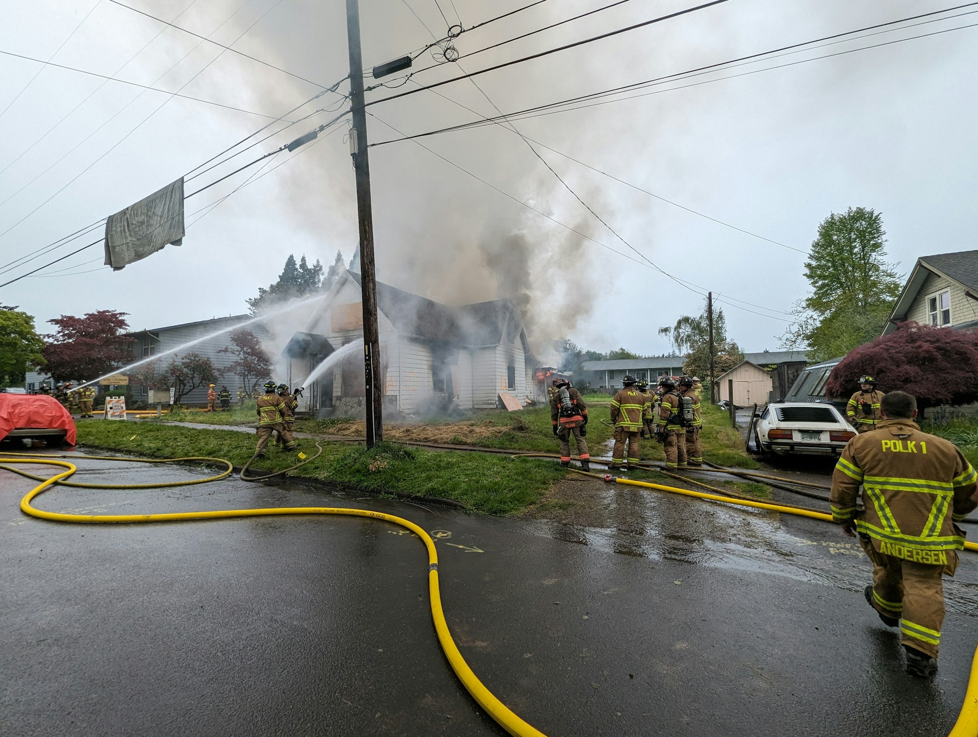 Firefighters combating a house fire, with hoses and smoke visible.