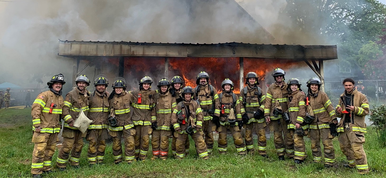 Firefighters posing in front of a burning structure.