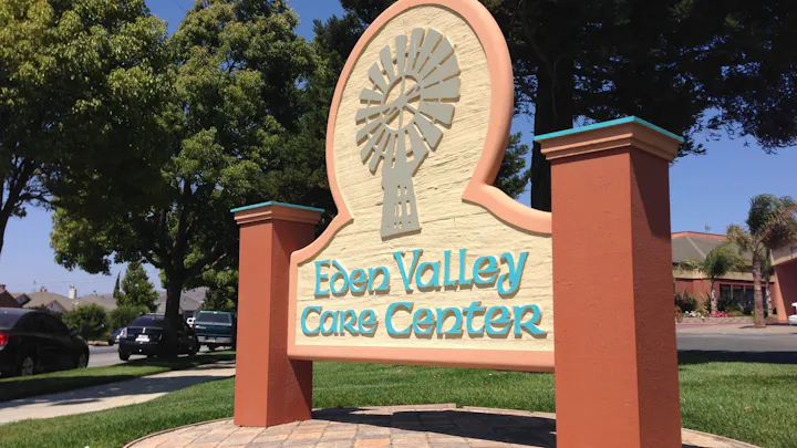 A sign reading "Eden Valley Care Center" with a windmill graphic, trees, and a clear blue sky.
