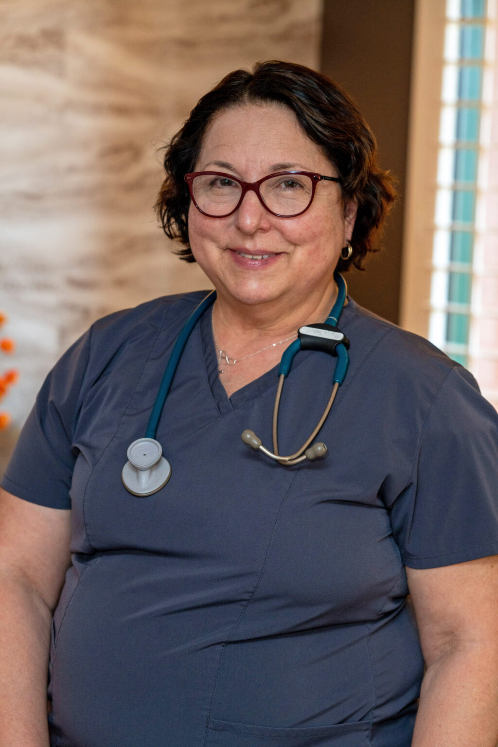 Photo of Maria E. Schell wearing a grey scrub top and a statoscope and glasses