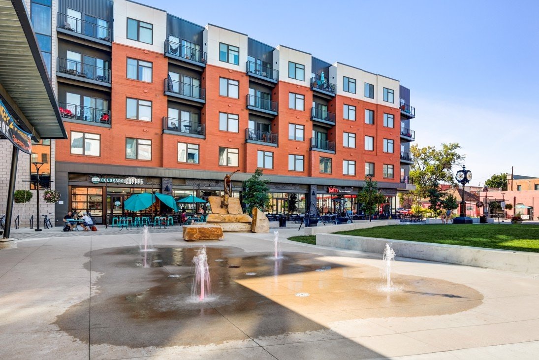 Modern building with shops, apartments, and a plaza with fountains.