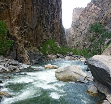 A scenic view of a river flowing through a narrow canyon, surrounded by steep rocky cliffs and some greenery.