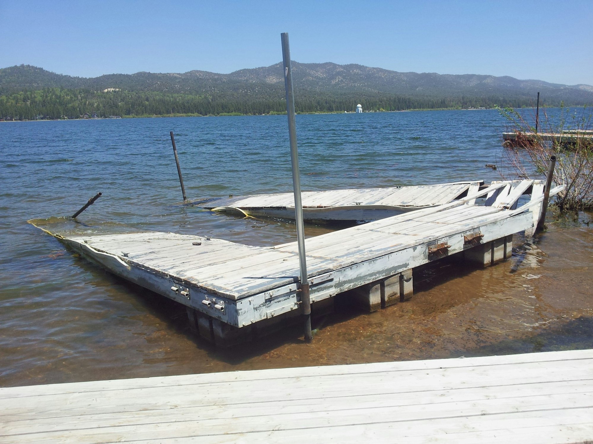 A weathered wooden dock on a lake with mountains in the background and clear skies above.