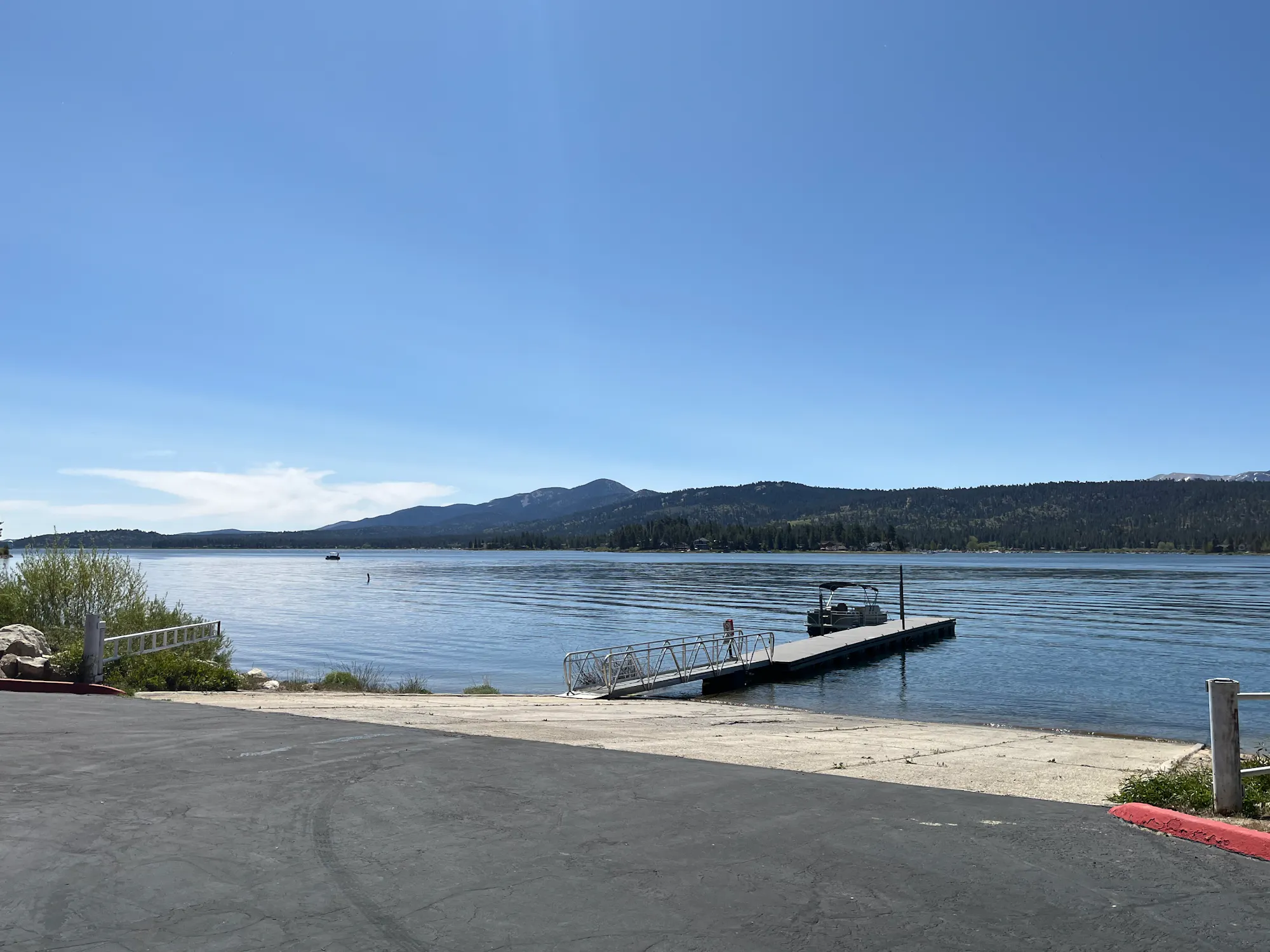 A serene lakeside view with a dock and boat, surrounded by mountains under a clear blue sky.