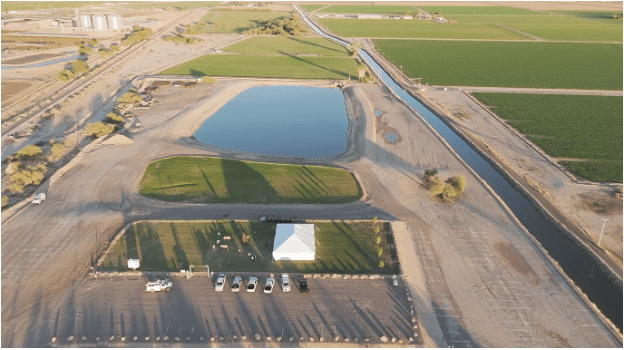 Aerial view of a water reservoir, parking area, tent, and green fields.