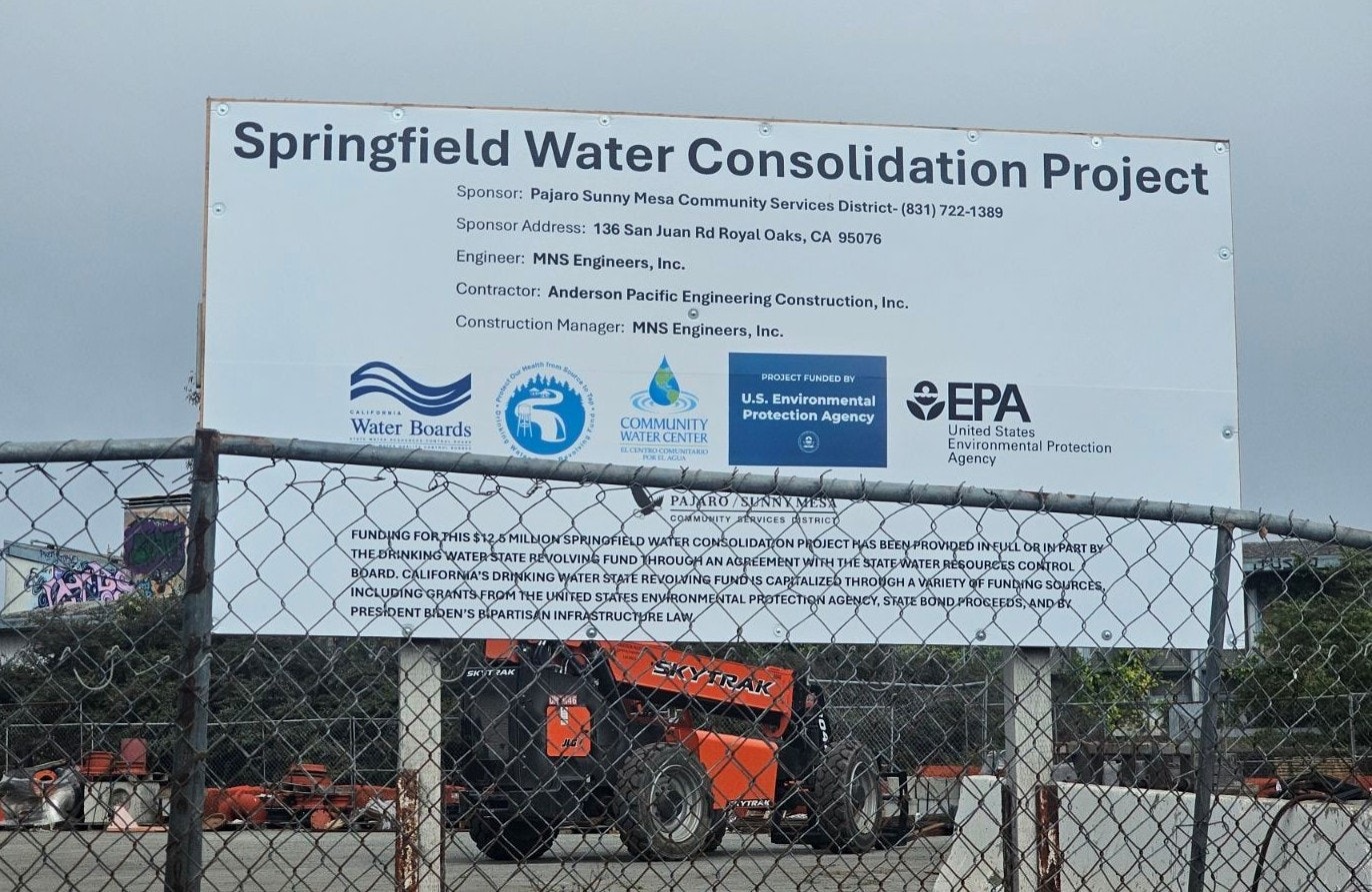 The image features a sign for the Springfield Water Consolidation Project, detailing sponsors, engineers, and funding sources.