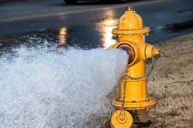 A yellow fire hydrant spouting a strong stream of water, with a wet ground nearby.