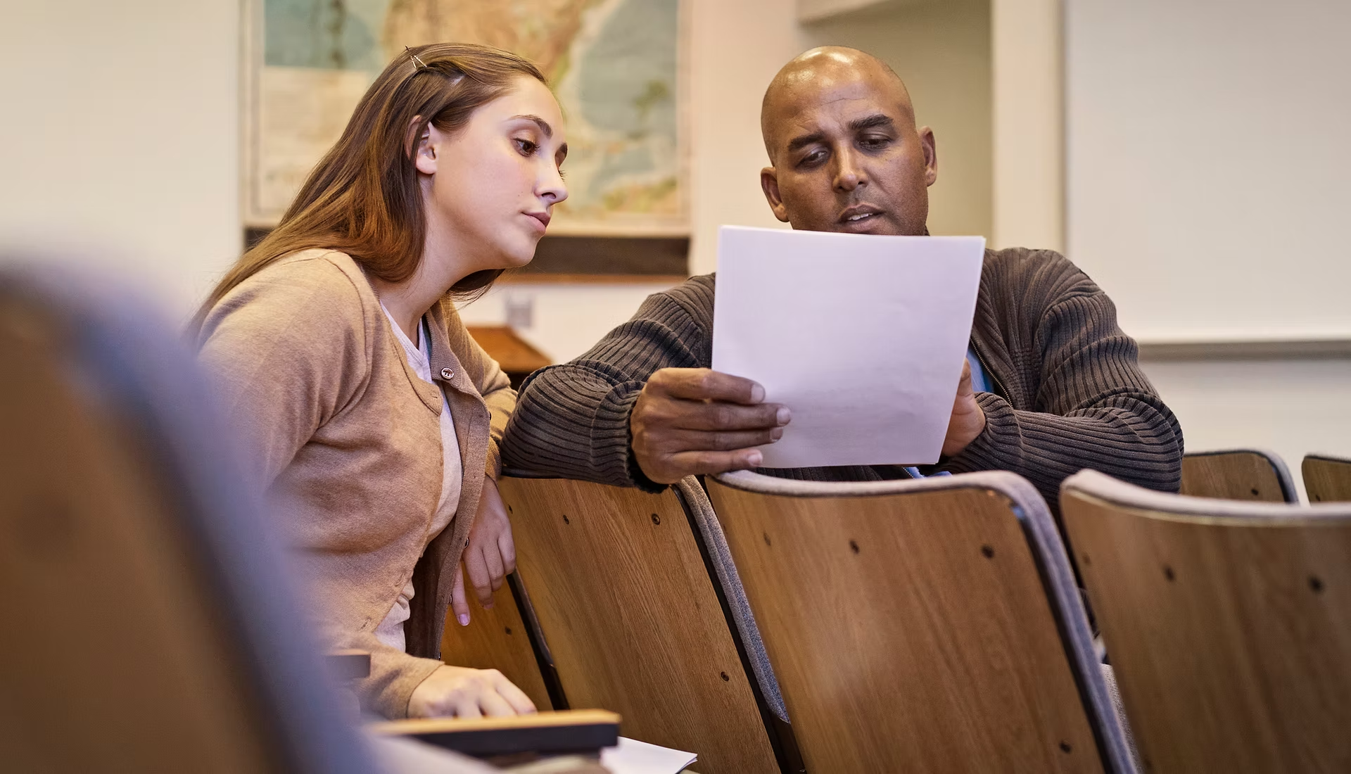 Two people are sitting in a lecture hall, discussing a document together.