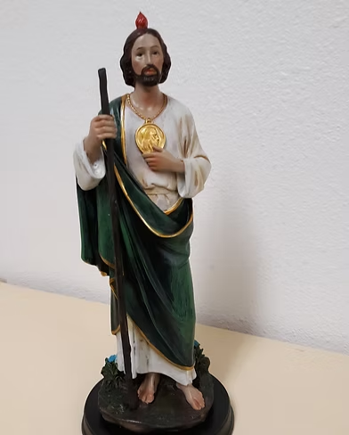 A statue of a bearded man holding a staff, wearing a green robe with gold accents, and featuring a heart symbol on his chest.