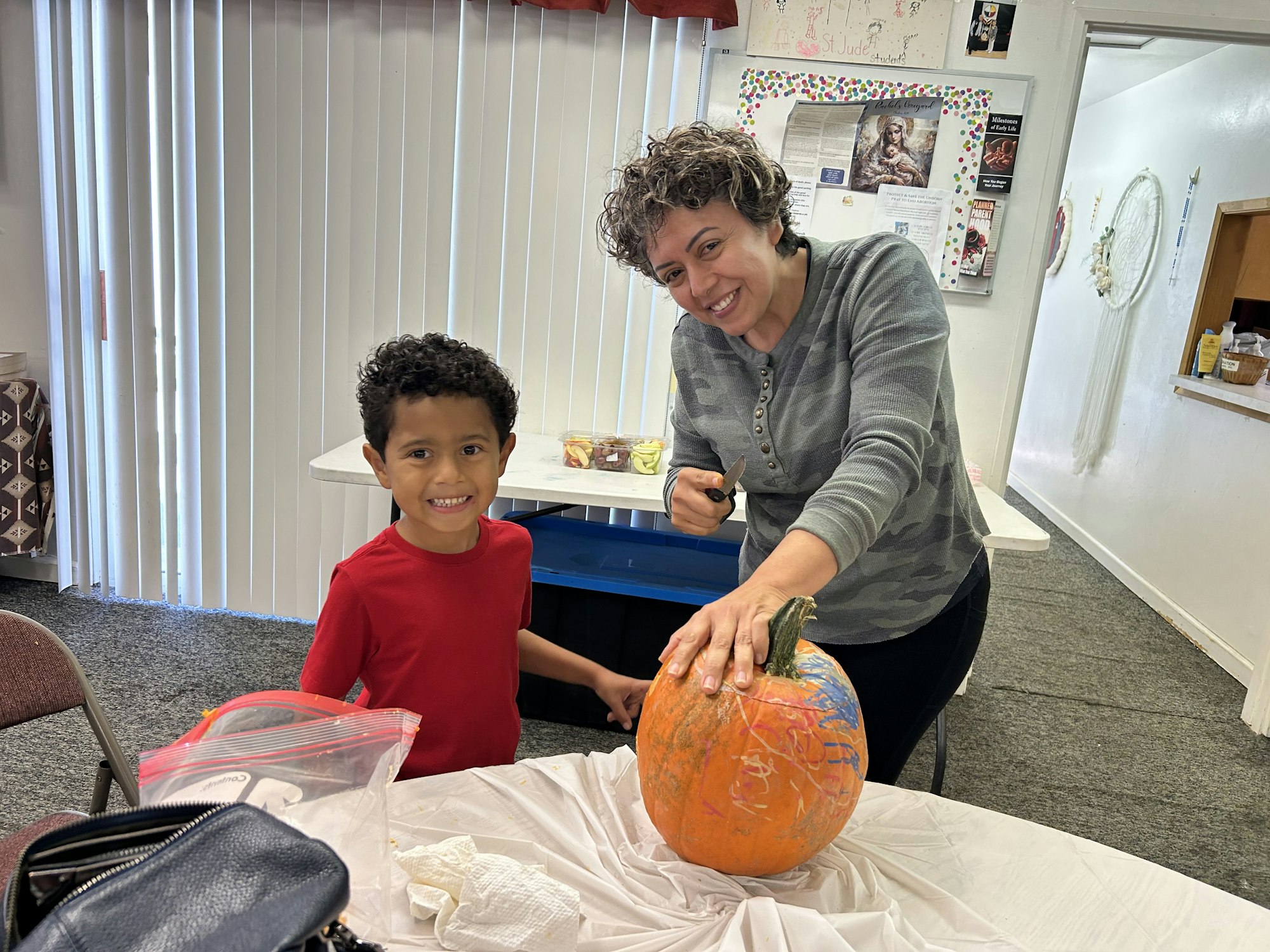 A smiling boy and woman are painting a pumpkin together in a cozy indoor setting.