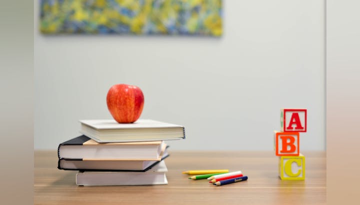 Books stacked with an apple on top, colored pencils, and ABC blocks on a table.