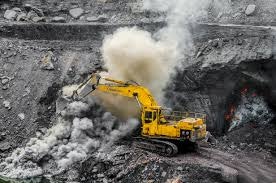 A yellow excavator works in a mining site, creating dust and smoke as it digs into the earth.
