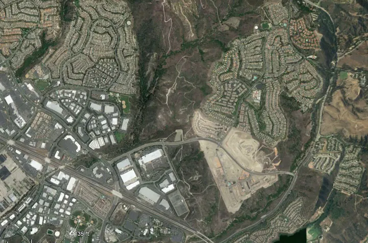 The image shows a satellite view of a suburban area featuring residential neighborhoods, commercial spaces, and some undeveloped land.