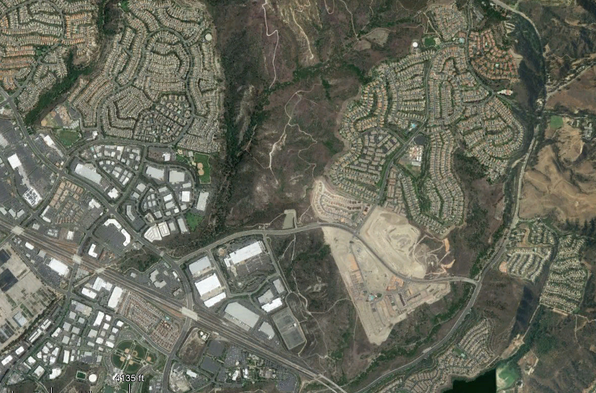 The image shows a satellite view of a suburban area featuring residential neighborhoods, commercial spaces, and some undeveloped land.