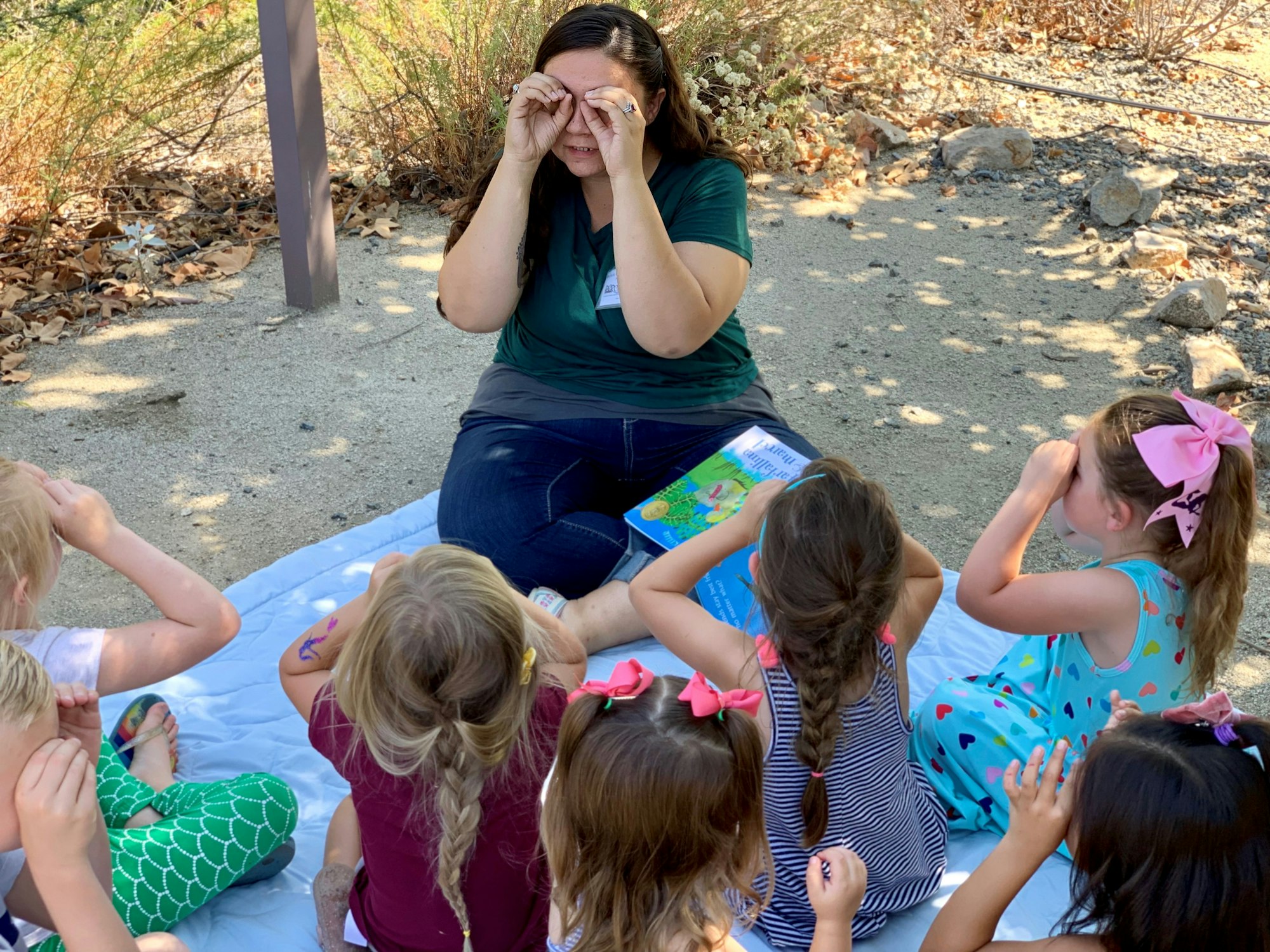 Image of naturalist sitting outside on a blanket with students.