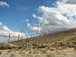 The image features a row of wind turbines on a hillside under a partly cloudy sky, representing renewable energy.