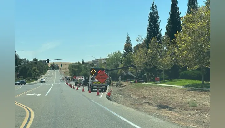 Road construction ahead with a closed lane sign, traffic cones, and equipment visible along the side of the street.