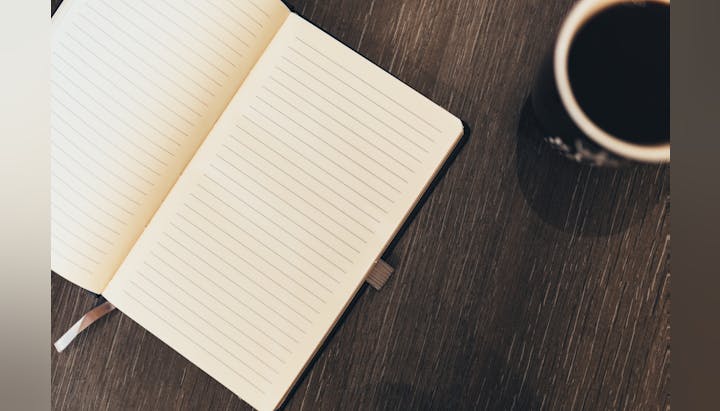 Open notebook with lined pages on a wooden surface, next to a cup of black coffee.