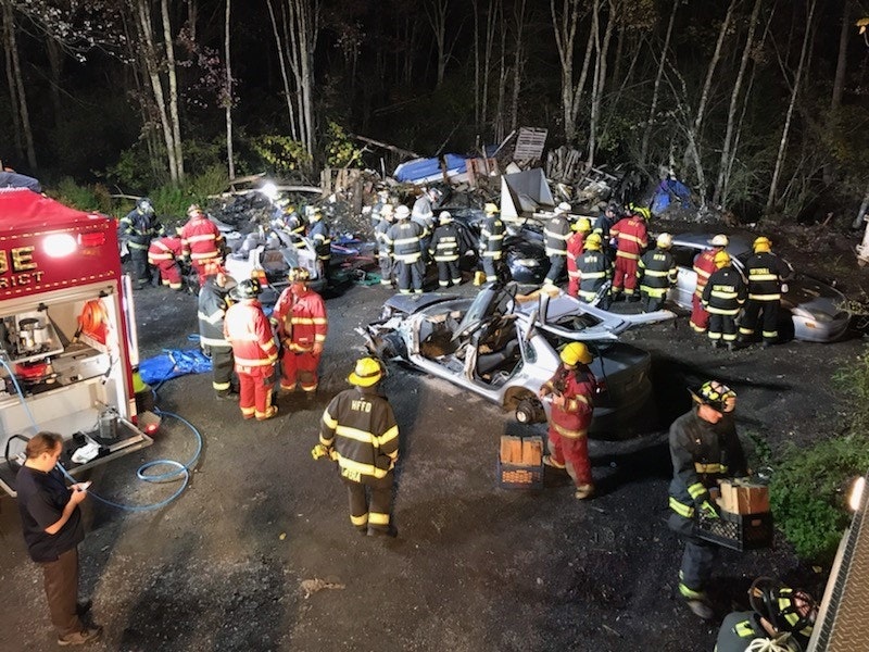 Firefighters at a night scene with a damaged vehicle and debris.