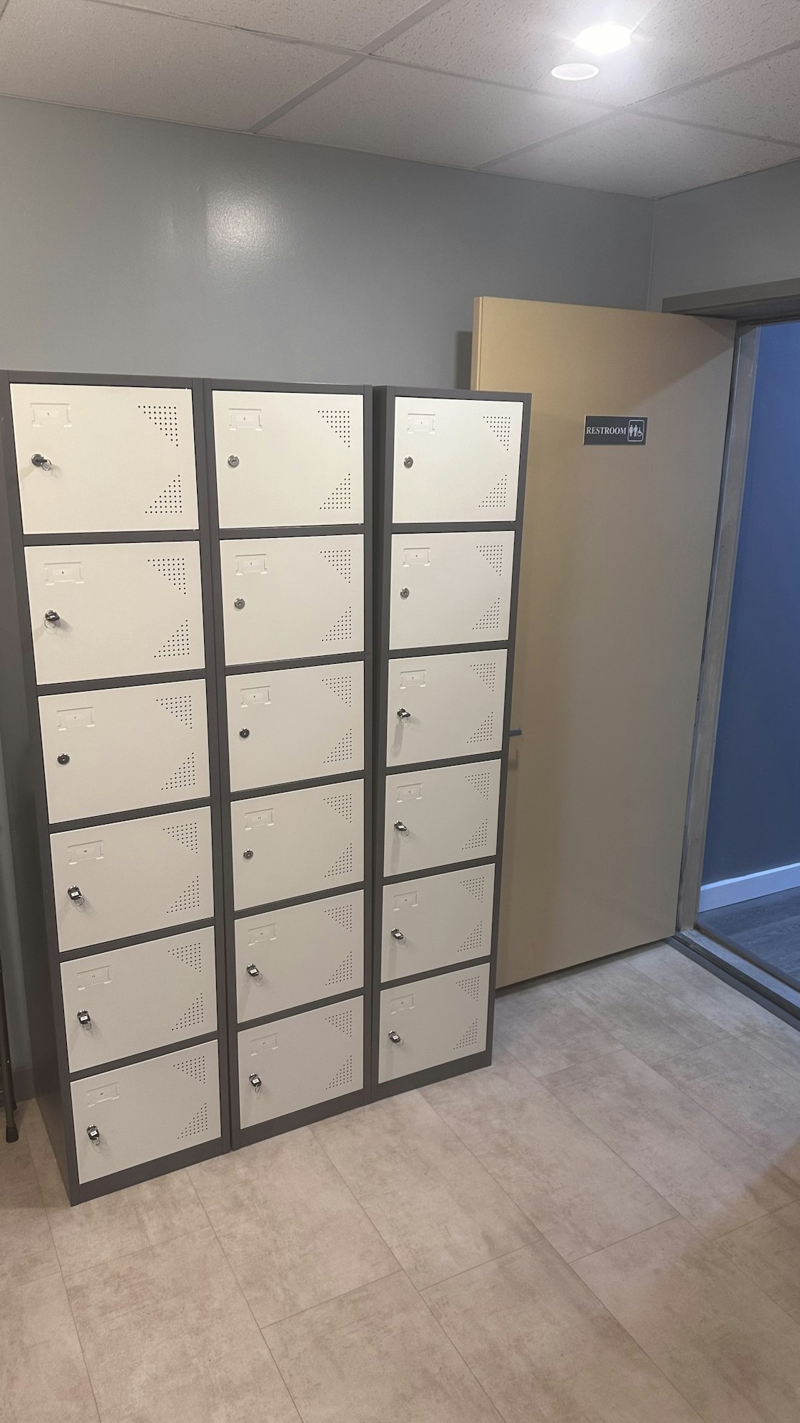 A row of lockers by a restroom entrance in a hallway.