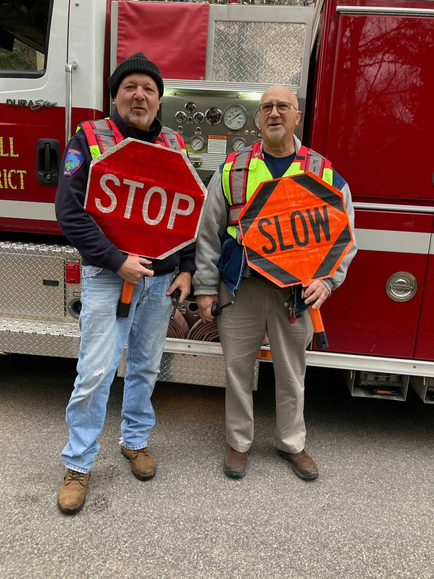 Two men with "STOP" and "SLOW" signs standing in front of a fire truck.