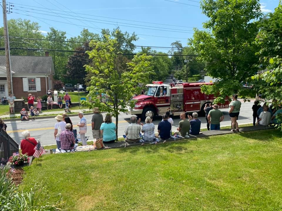 A community gathering watching a parade with a fire truck passing by on a sunny day.