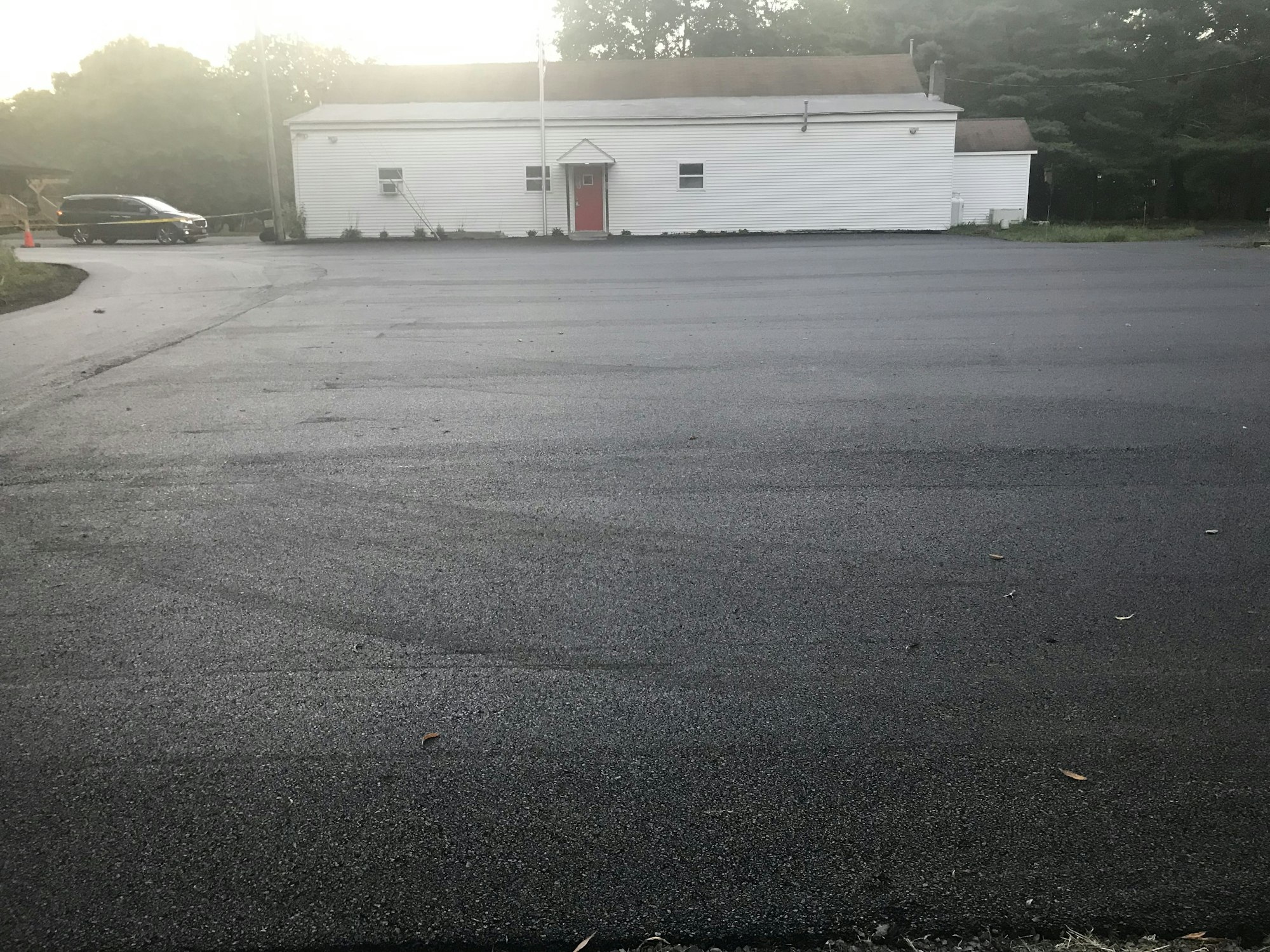 A parking lot with a white building, red door, and a car in the distance.