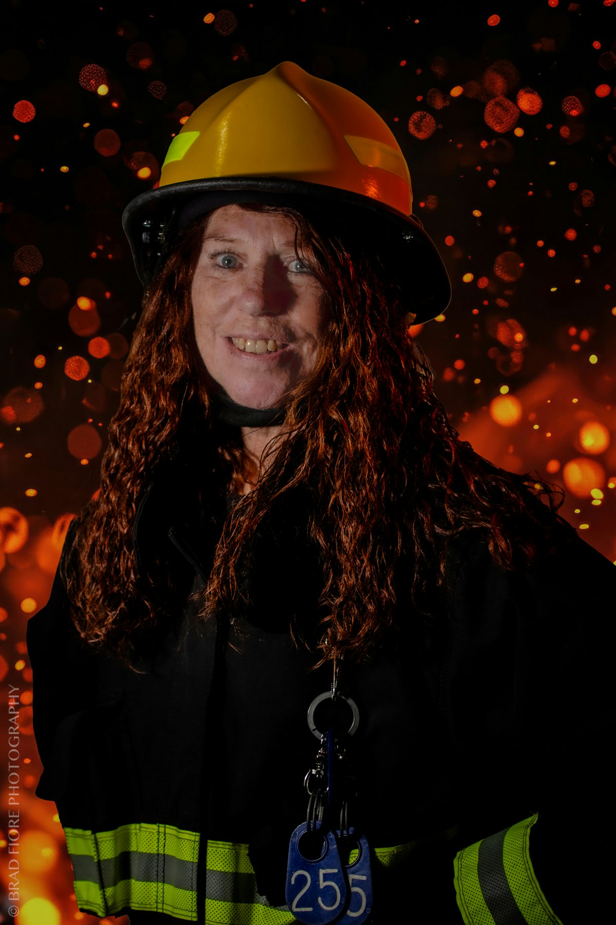 Person wearing firefighter gear with a yellow helmet, smiling against a fiery background.
