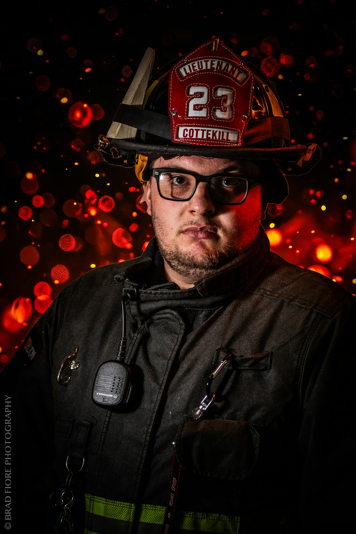 A firefighter wearing a helmet and uniform, with a bokeh effect of red lights in the background.