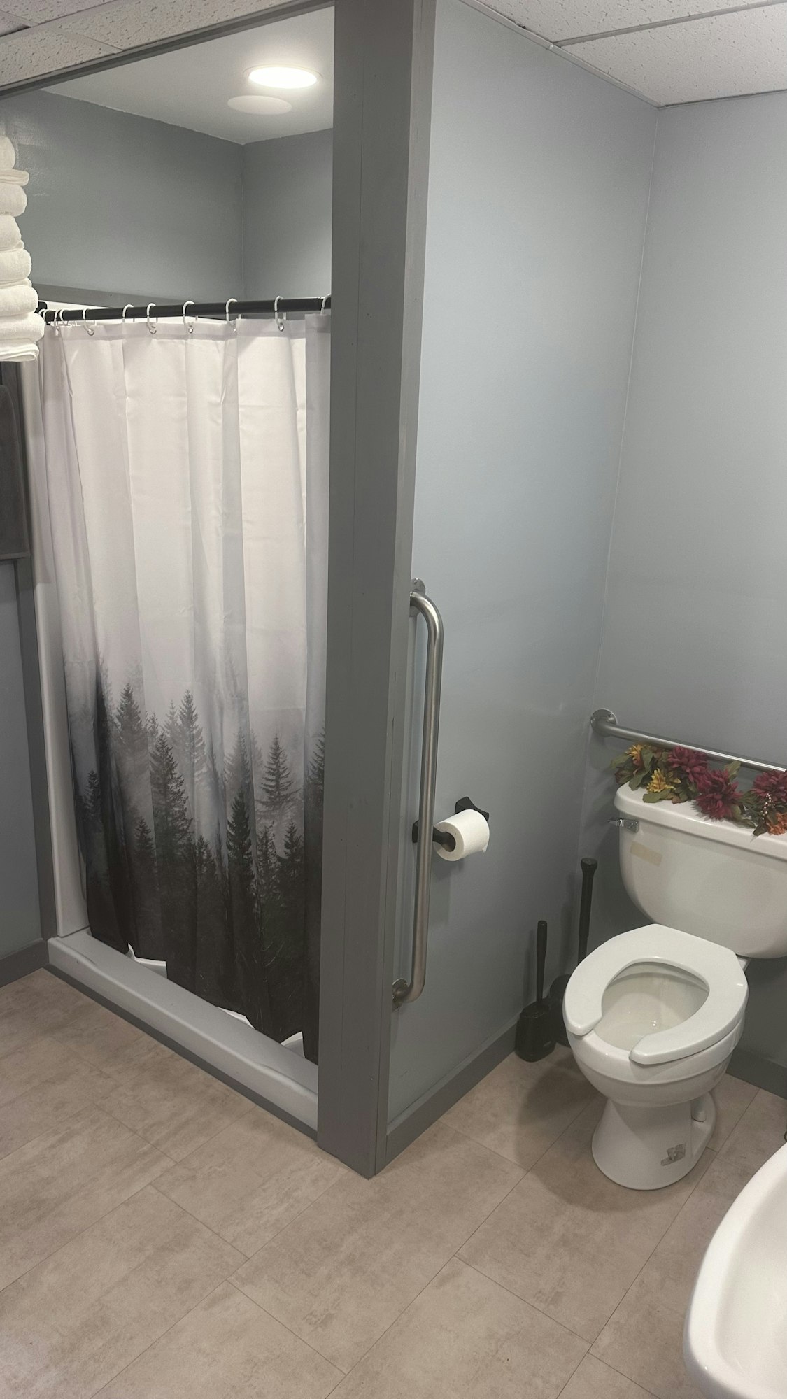 A bathroom with a shower, toilet, floral decoration, and a plunger.