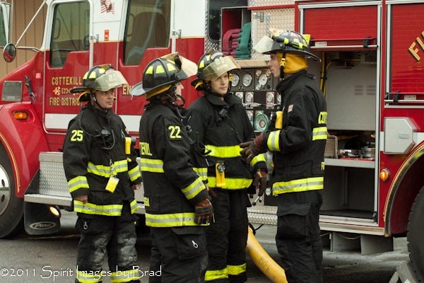 Firefighters in gear conversing near a fire truck.