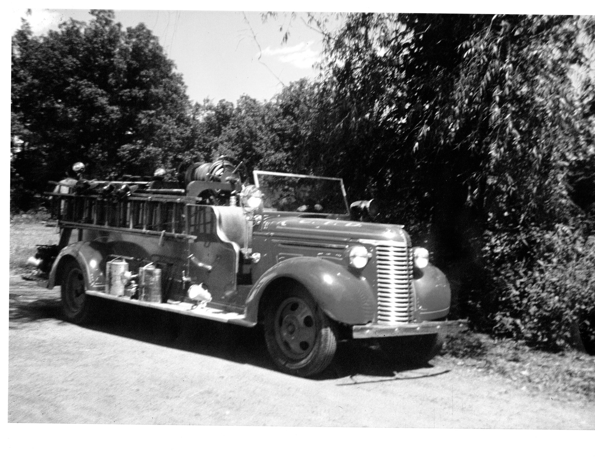 Vintage fire truck with firefighters on board, outdoors in daylight.