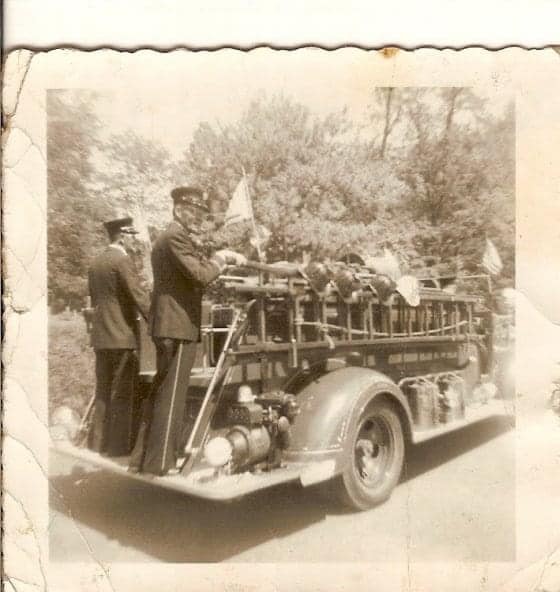 Vintage photo of people on an old fire truck, possibly in a parade.