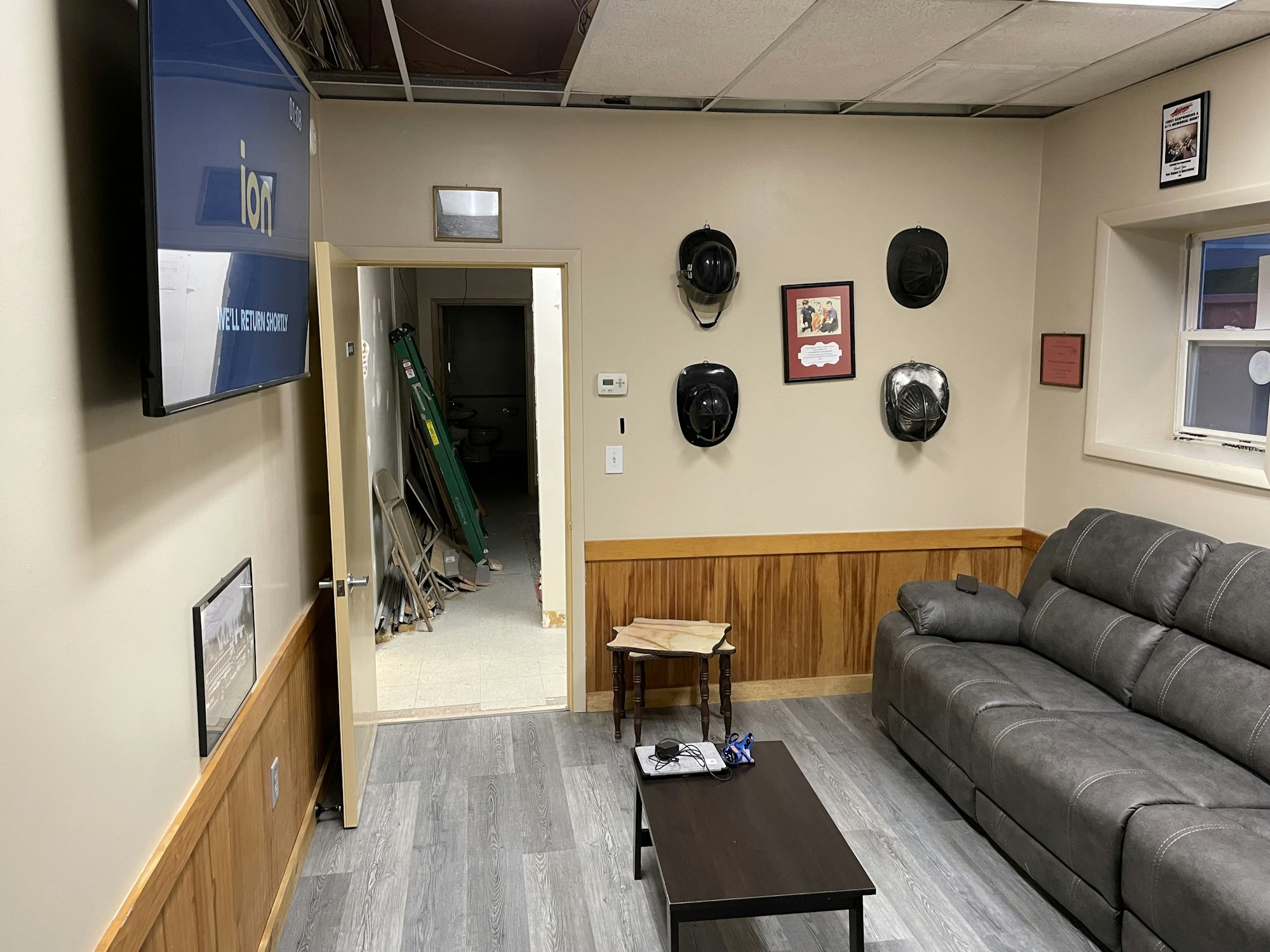 A waiting room with a couch, TV, firefighting helmets on the wall, and a hallway with folding chairs.